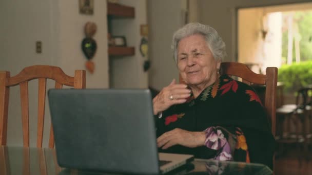 積極的な高齢女性を身に着けている暖かい服でテーブルに座っていると空気のキスを送信しながらビデオ通話で話しますラップトップを使用して — ストック動画
