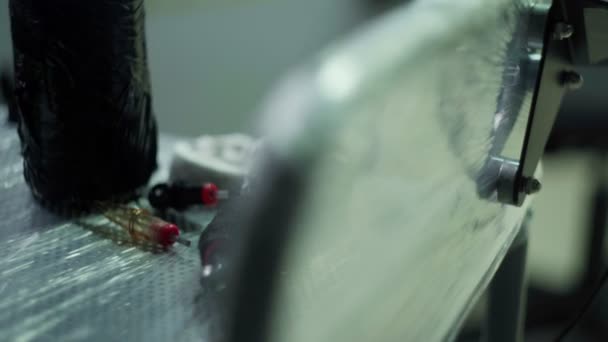 軽い入れ墨のスタジオのコトン近くのクローリングフィルムで覆われた金属表面に置かれたプロのブラックタトゥーマシンの高角度 — ストック動画