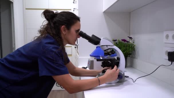 穿蓝色制服的女兽医在实验室工作时透过显微镜的侧视图 — 图库视频影像
