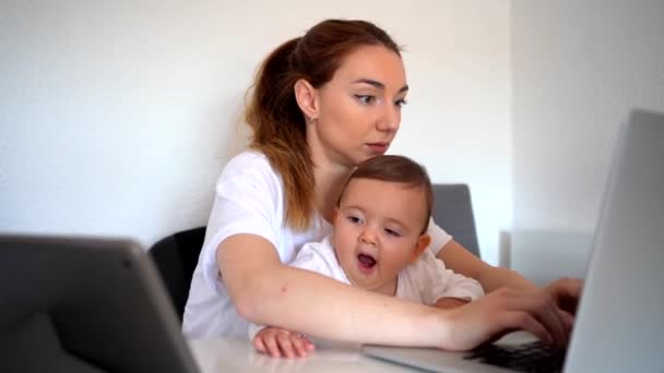 Орієнтована Молода Мати Працює Ноутбуці Тримаючи Допитливу Дитину Дивлячись Смішне — стокове відео