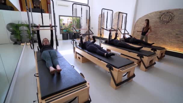Kompania Kobiet Odzieży Sportowej Reformatorach Pilates Podczas Szkolenia Pod Nadzorem — Wideo stockowe