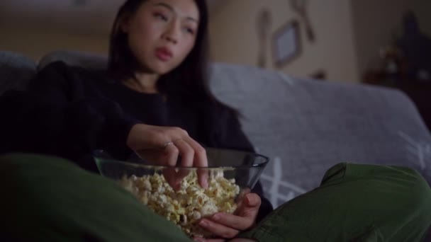 Młoda Azjatka Luźnych Ciuchach Siedząca Skrzyżowanymi Nogami Kanapie Jedząca Popcorn — Wideo stockowe
