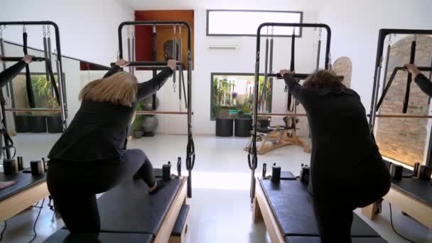 一组柔韧女性在教练员控制下在普拉提改革者上伸展腿的背景图 — 图库视频影像