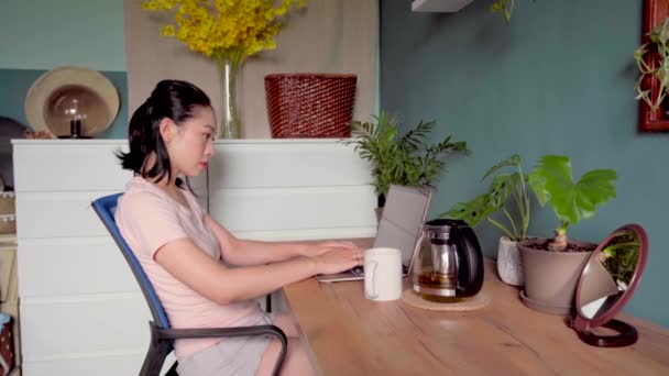 リモートワーク中にテーブルに座っている間 ラップトップ上の文書を読むアジアの女性のフリーランスの側面図 — ストック動画