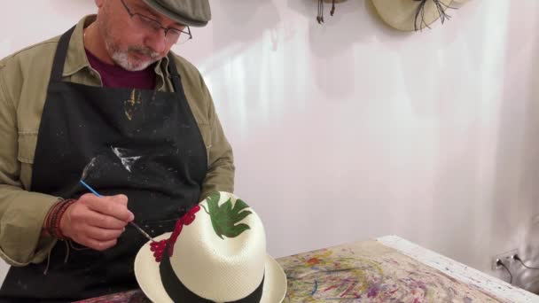 ワークショップでスタイリッシュなわら帽子にブドウの装飾を作成しながら エプロンと眼鏡で注意深い成熟した男性アーティストをクロップ — ストック動画
