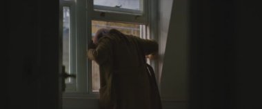 Kahverengi paltolu kadın pencereden dışarı adımını atıyor.