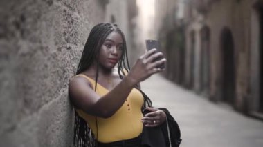 Siyah takım elbiseli Afro-Amerikan bir kadının akıllı telefonuyla sokakta durup selfie çekerken çekilmiş görüntüleri. 