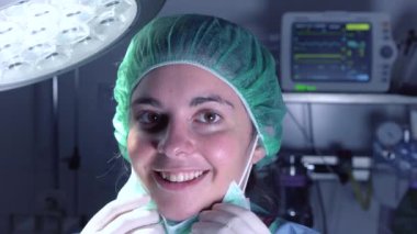 Tıbbi maskeli ve şapkalı yetişkin bir kadın hastanede ameliyat yapmadan önce kameraya bakıyor.
