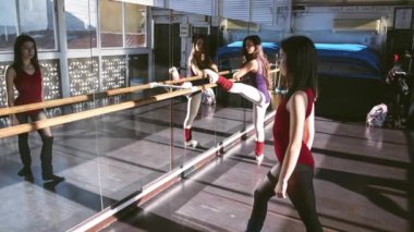 Genç kızlar ayna önünde parlak bir stüdyoda dans ediyorlar. Yavaş çekim, yumuşak hareket. Modern dans kavramı