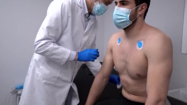 ECG testi için tanınmayan bir erkek hastanın göğsüne elektrot uygulayan ekin doktoru.