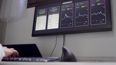 Bilgisayarda çalışan tanınamayan bir kadın. İşyerinde kripto para biriminin değerindeki değişimleri gösteren grafiklerle çalışıyor.