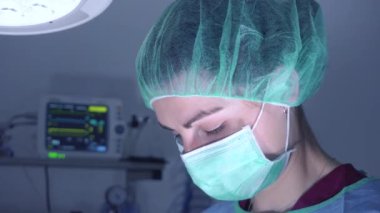 Ameliyathanede parlak ışık altında dururken profesyonel aletler kullanan tıbbi üniformalı bir kadın. 
