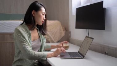 Genç etnik kadın blogcu elinde netbook ve kahveyle oturma odasındaki ekrana bakıyor. 