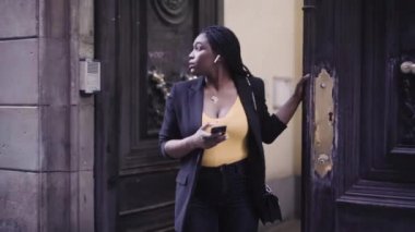 Siyah takım elbiseli genç Afro-Amerikan bir kadının akıllı telefonuyla sokakta yürüdüğü görüntüler. 