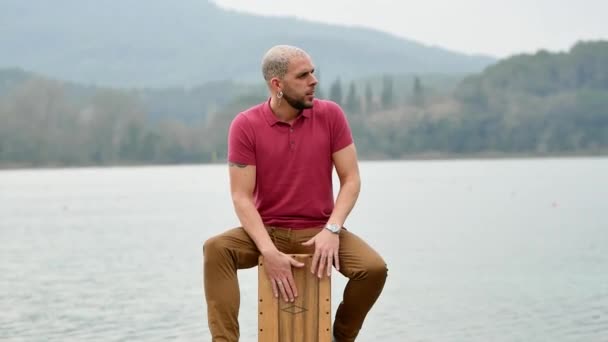 Percusionista Masculino Concentrado Sentado Jugando Cajón Muelle Madera Contra Río — Vídeos de Stock