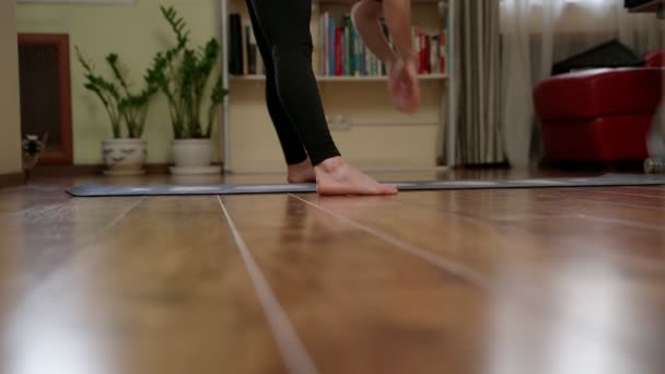 自宅でのヨガトレーニング中にストレッチしながらマットの上に立っているスポーツウェアの柔軟な女性のリアルタイムフルボディ — ストック動画