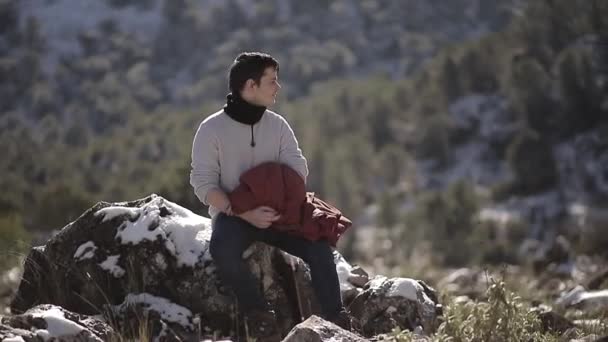 穿着保暖衣服的年轻男性游客坐在石头上 靠着山凝视着阳光 凝视着大自然 — 图库视频影像