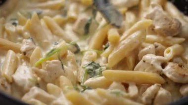 Evdeki modern mutfakta öğle yemeği pişirirken kremalı ıspanaklı rigatoniyi karıştıran isimsiz biri.