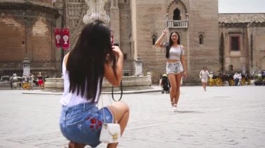 Arka planda, Sevilla, İspanya 'da gülümseyen kız ve katedralin fotoğraflarını çeken Çinli kadın turist var.