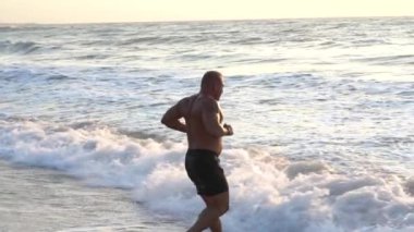 Gün batımında deniz kıyısındaki yakışıklı kaslı adamın silueti.