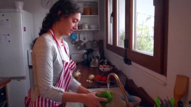 Mutfakta genç bir kadın kırmızı ve yeşil biber yıkıyor.