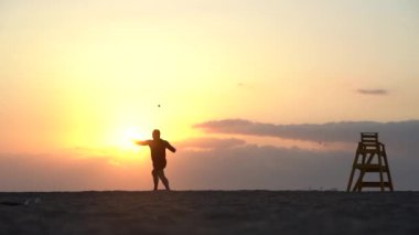 Gün batımında deniz kıyısındaki yakışıklı kaslı adamın silueti.