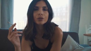 Genç esmer kadın odada sigara içiyor.