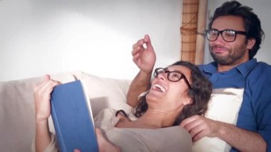 Genç çift kitap okuyor ve kanepede sarılıyorlar.