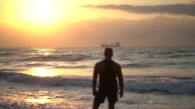 Gün batımında deniz kıyısındaki yakışıklı kaslı adamın silueti.