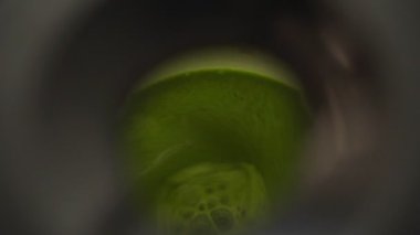 Yukarıdan gelen isimsiz kişi mutfakta sağlıklı bir içecek hazırlarken köpüklü yeşil smoothie ile karıştırıcıyı açıyor.