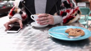 Süveterli bir kız kafede oturuyor ve akıllı telefon kullanıyor. 