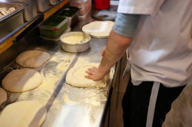 Bir pizzacının masasında elle pizza yaparken tanınmayan bir fırıncının ellerinin detaylı görüntüsü.