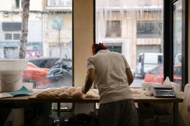 Beyaz tişört giymiş, kırmızı şapkalı fırında sırtı kameraya dönük olarak çalışan tanınmamış bir fırıncı.