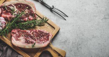 Biberiyeli çiğ biftek arka planı ve ahşap kesme tahtasındaki yeşil biberli ve kasap çatallı. Kapatın. Taze et hazırlanıyor. Kopyalama alanı olan üst görünüm.