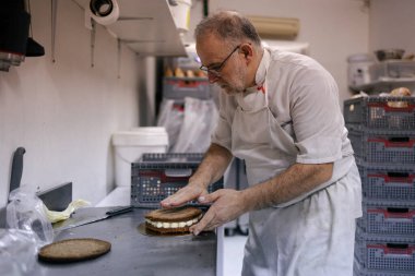 Beyaz önlüklü, beyaz saçlı, fırın mutfağında pasta yapan kıdemli pasta şefi.