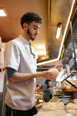 Beyaz önlüklü genç bir Arap pizzacı pizzacının mutfağında elle yoğuruyor.