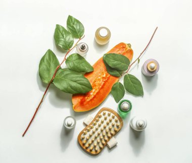 Yarım papaya, güzellik ürünleri, kuru masaj fırçası ve beyaz arka planda yeşil yapraklı vücut bakımı kozmetik seti. Sürdürülebilir güzellik cilt bakımı kavramı. Üst görünüm.
