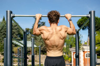 Sarışın, yakışıklı genç adam güneşli bir günde açık hava spor salonunda barfiks çekiyor.