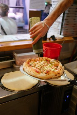 Napoli pizzası fırından yeni çıkmış kürekle. Tanınmayan bir pizzacı pizzacıya sos eklerken..