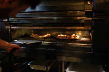 Tanımlanamayan pizzacı fırındaki iki pizzayı elinde kürekle kontrol ediyor.