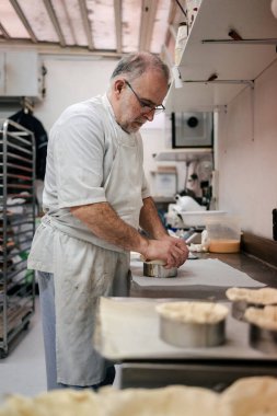 Beyaz önlüklü ve gözlüklü kıdemli pasta şefi bir pastanenin mutfağında pasta yapıyor.