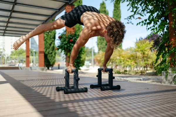 Sarışın, yakışıklı genç adam güneşli bir günde paralel barlarda planche yapıyor.
