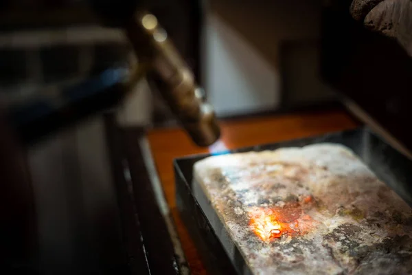 Jeweler melting silver metal with open flame blow torch welding.