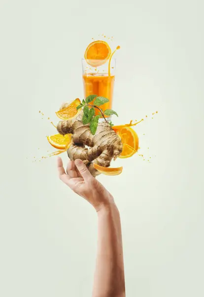 Women hand holding balancing ginger and orange immunity boosting drink with splashing and ingredients at light background. Creative healthy lifestyle. Levitation food . Front view