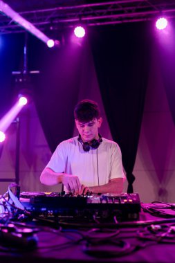 Genç bir DJ 'in bir kulüpte elektronik müzik çalarken çekilmiş dikey fotoğrafı.