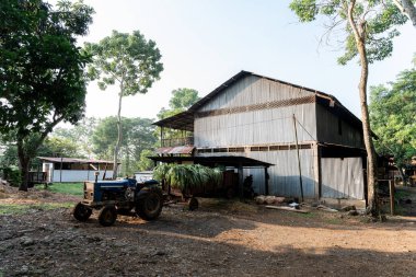 Doğal ortamda bir traktör, römork ve ahırın yer aldığı kırsal bir sahne.