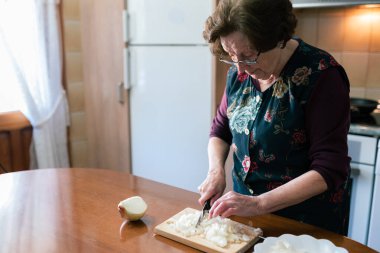 Evde kroket hazırlamak için bıçakla soğan doğrayan yaşlı bir kadının fotokopi çekilen yatay fotoğrafı.
