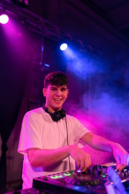 Renkli neon ışıklı bir gece kulübünde çalışırken kameraya gülümseyen mutlu bir DJ 'in dikey portresi