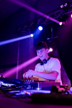 Genç ve mutlu bir DJ 'in dikey fotoğrafı. Mor neon ışıklarla bir diskoda karışıyor.