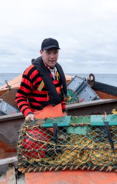 Kafkasyalı genç bir balıkçının dikey portresi bir teknede çalışmaya hazır kameraya bakıyor.